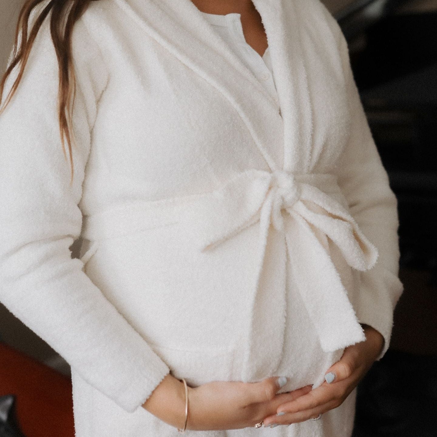 Person wearing a white robe holding their pregnant belly.