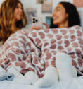 Load image into Gallery viewer, Two people sitting on a bed under a Little Giraffe blanket, smiling and looking at a phone.

