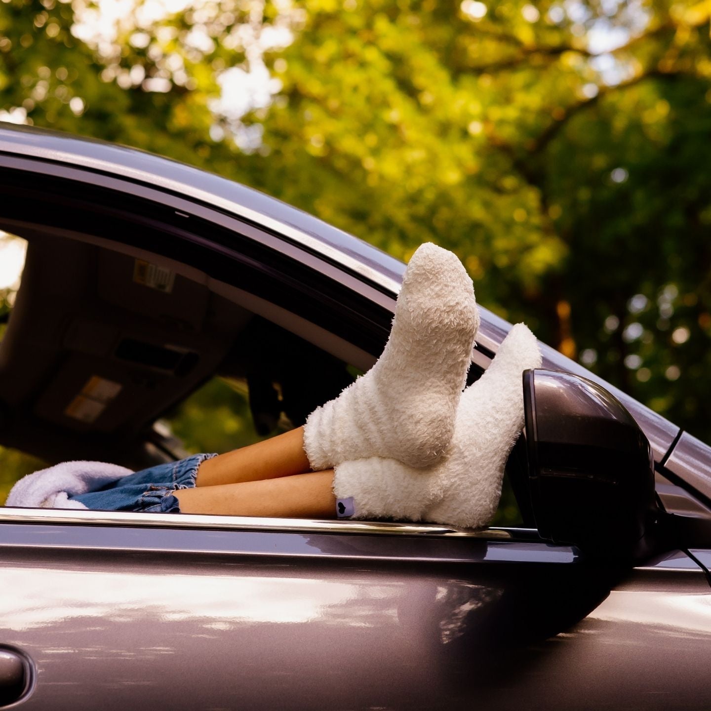 Person's feet in white socks sticking out of a car window with greenery in the background