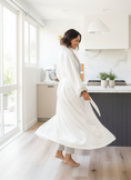 Load image into Gallery viewer, Woman in a white robe standing in a modern kitchen.
